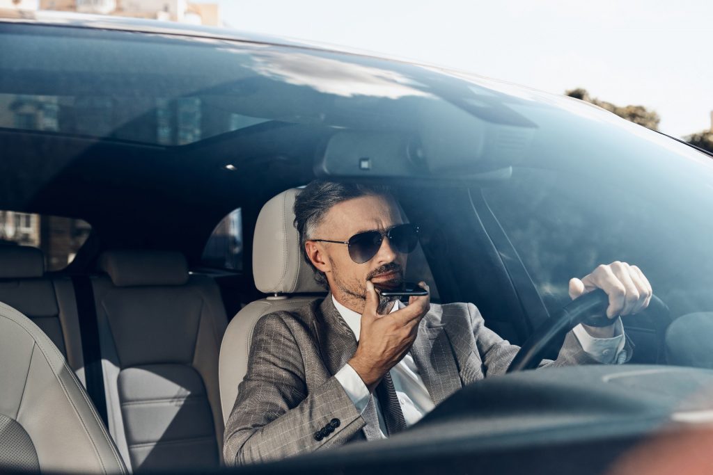 Hombre de negocios con traje gris utilizando una aplicación de voz a texto mientras está sentado en su coche.