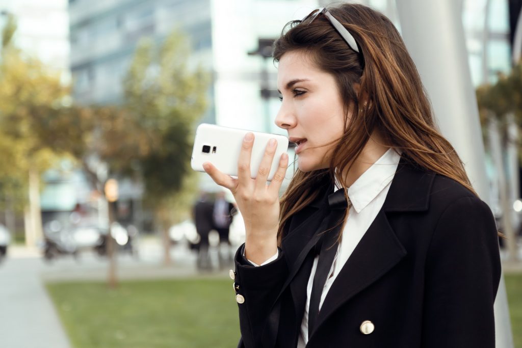 Geschäftsfrau, die auf ihrem Telefon eine App zur Umwandlung von Sprache in Text verwendet, während sie sich im Freien aufhält