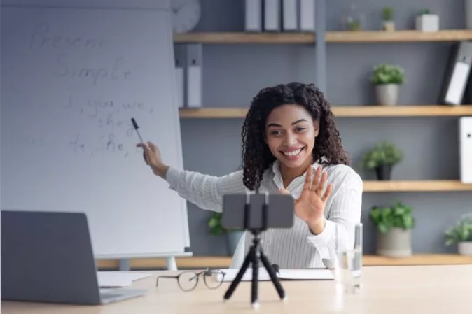 Frau, die einen Online-Vortrag per Webcam hält, mit einer physischen Tafel hinter ihr