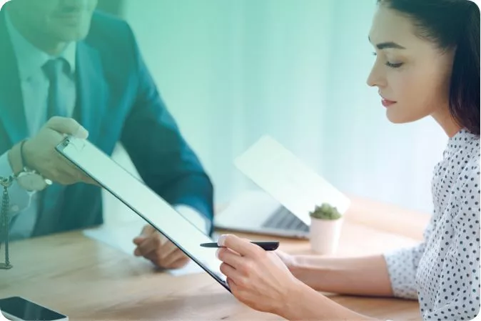 Woman in white shirt reading and signing a political document being handed to her by a man in a blue suit