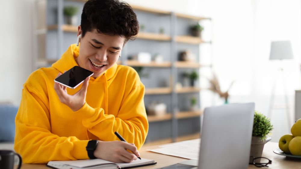 asian man with yellow sweater uses device to translate voice into text