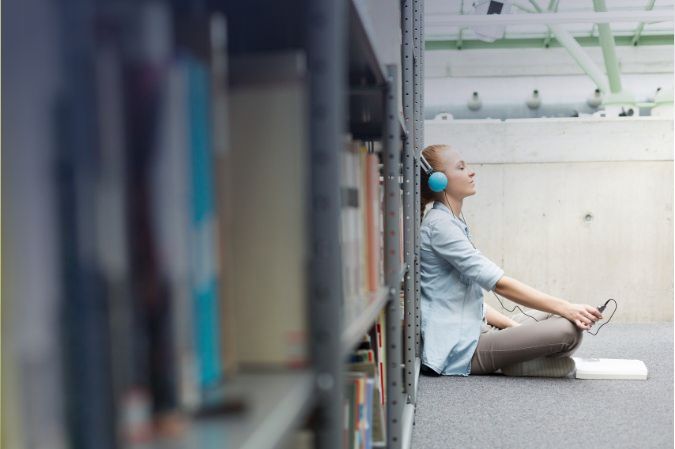 Woman listening to music sitting next to a bookshelf in a library