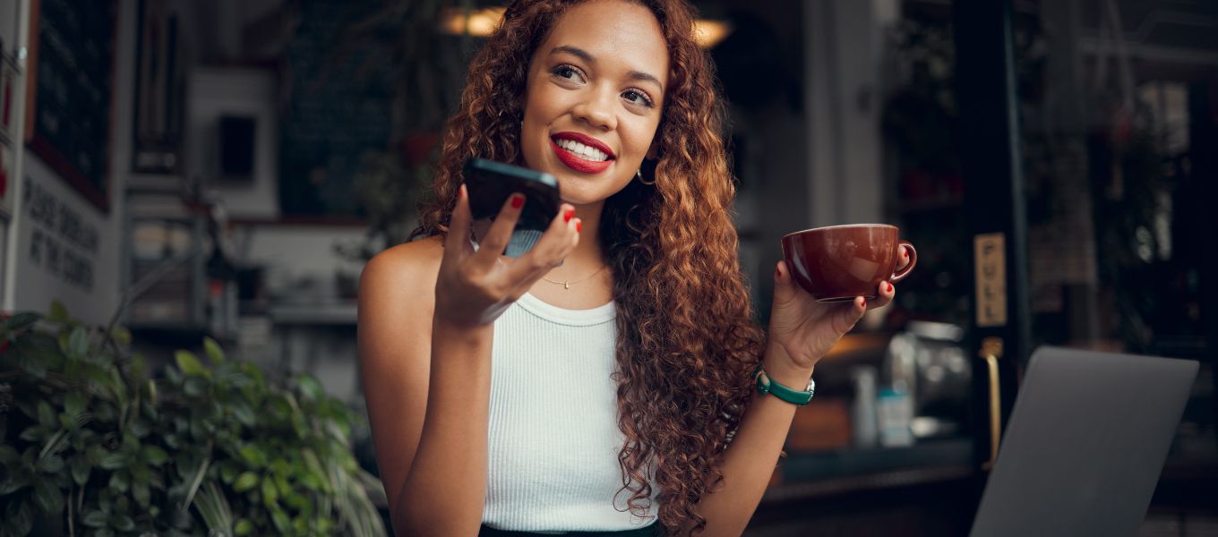 Pretty woman using speech to text on her phone in a café while drinking coffee