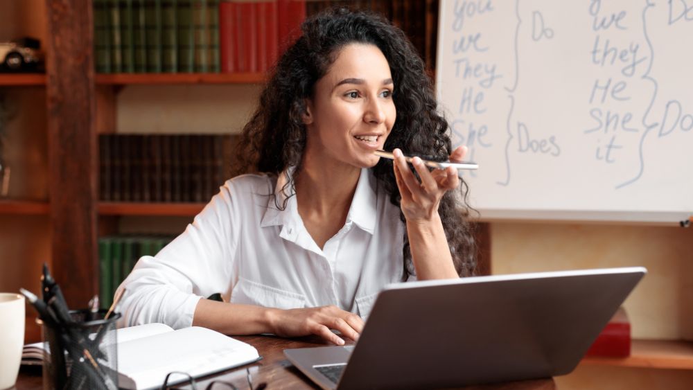 Woman in a white shirt talking through her phone on speakers in front of her laptop