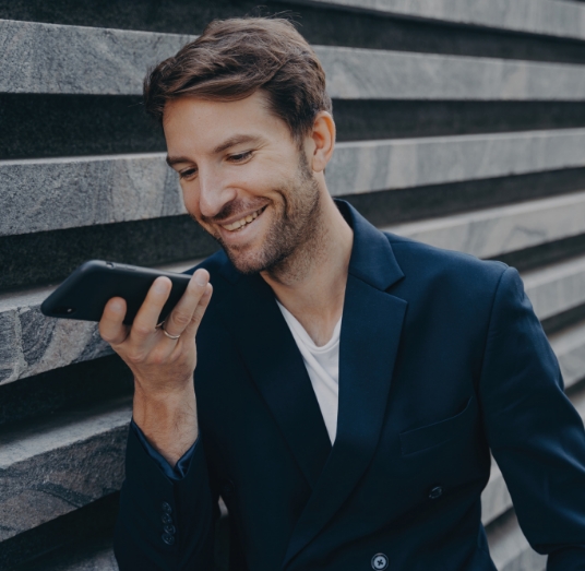 handsome man dictating to his phone leaning to a wall