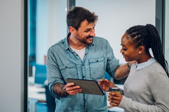 Man showing business info to female colleague with a tablet device in the office